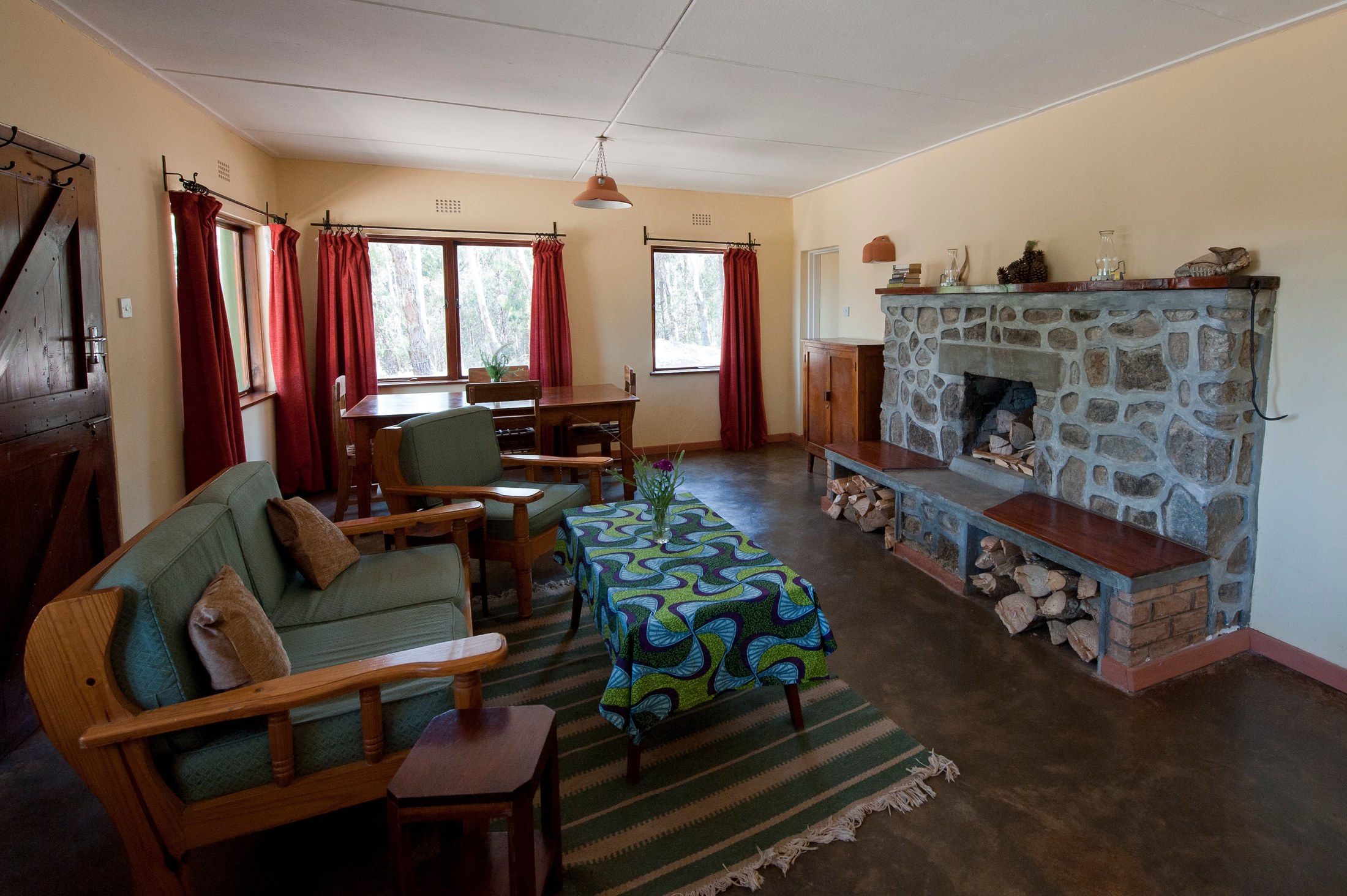 The lounge at Chelinda Camp, with armchairs, a stone fireplace and a dining table.