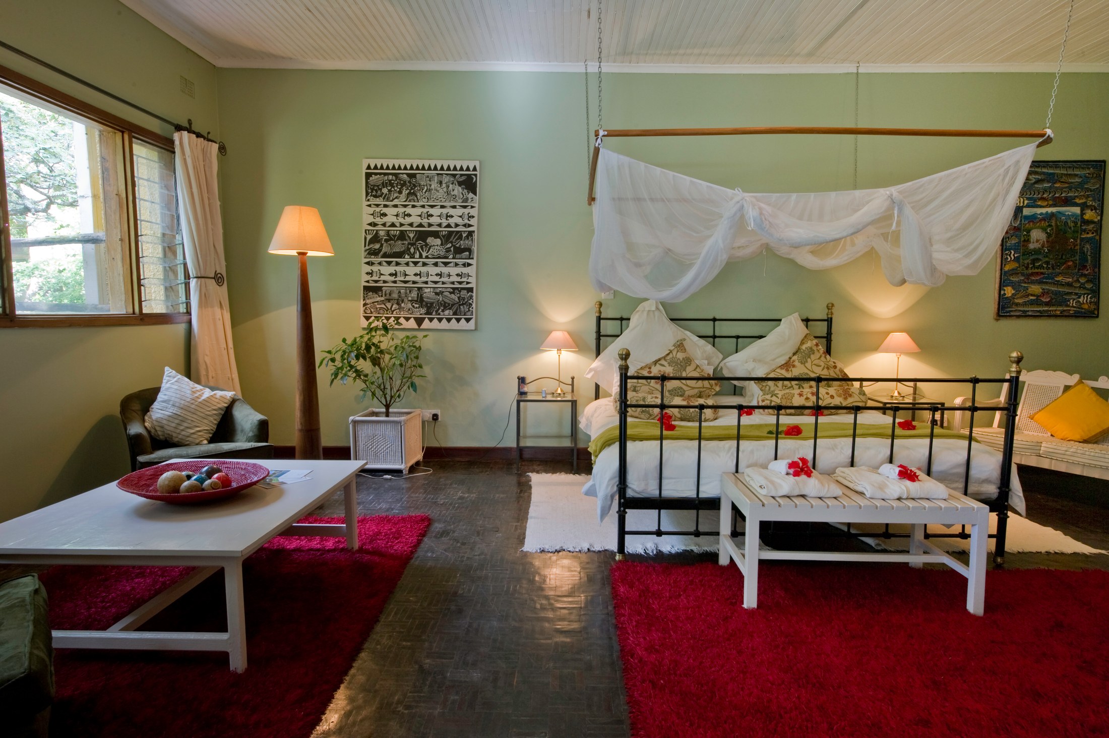 An airy Heuglin’s Lodge bedroom with a mosquito-netted bed, seating area and green walls.