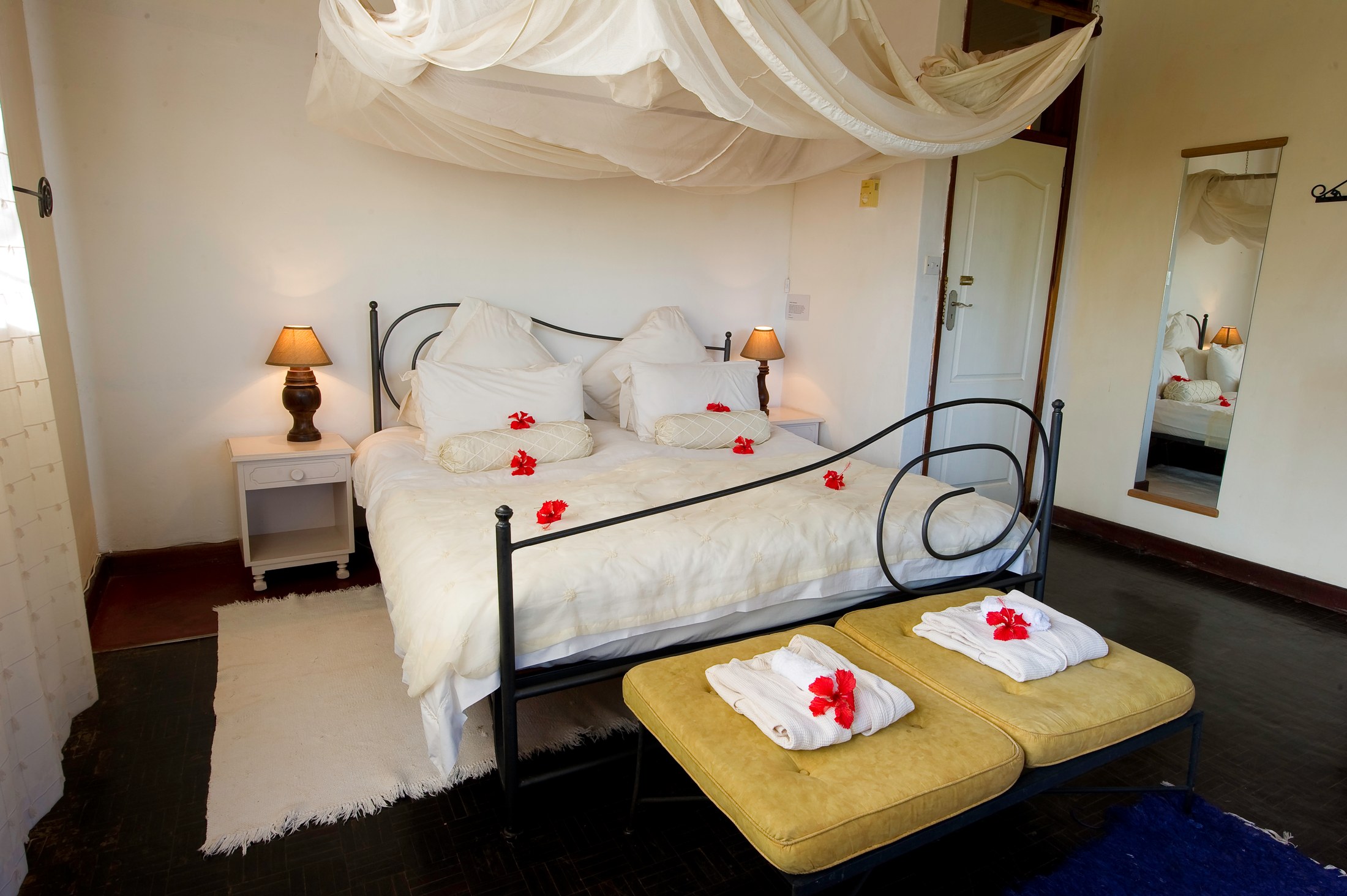 A double bedroom at Heuglin’s Lodge with white mosquito netting and bedside lamps.